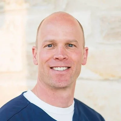 Chris Price smiling in front of a stone wall.